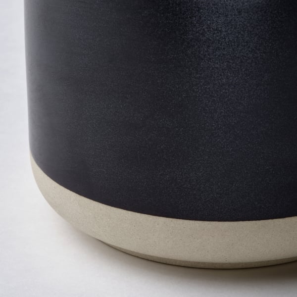 Close-up of a dark grey candle in a textured stoneware holder. The craftsmanship highlights a smooth, rounded edge.