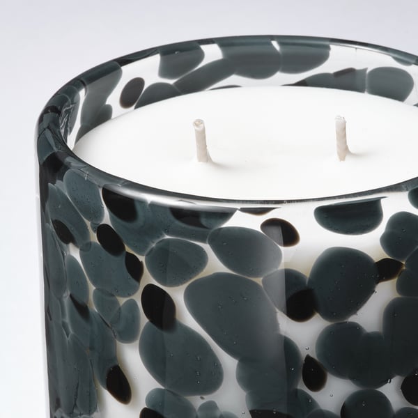Close-up of a multi-wick candle in a textured glass. Dark green spots on clear glass, three white wicks visible. Elegant, artisanal design.