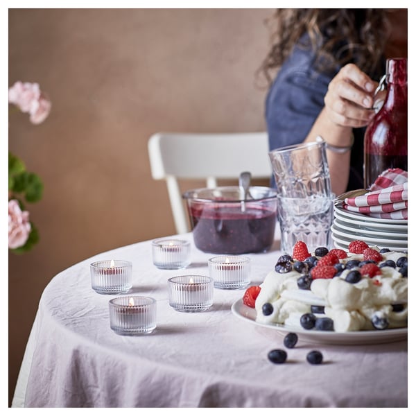 Table set with berry dessert, STÖRTSKÖN candles, glasses, stack of plates, and person pouring drink.