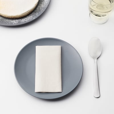 A table setting featuring a blue plate with a neatly folded white napkin, a metal spoon, and a glass of water. Perfect for serving dining or dessert.