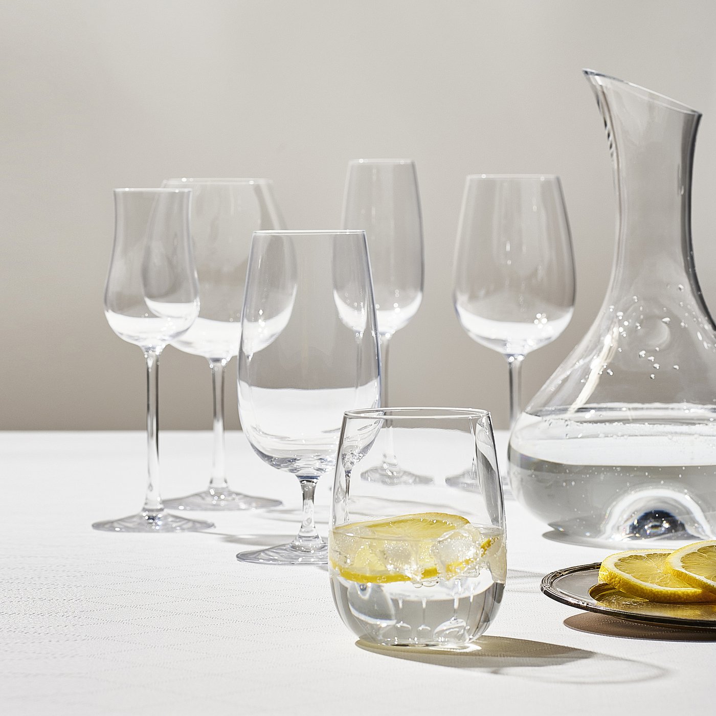 Six STORSINT crystal glasses and carafe on white tablecloth with lemon slices.
