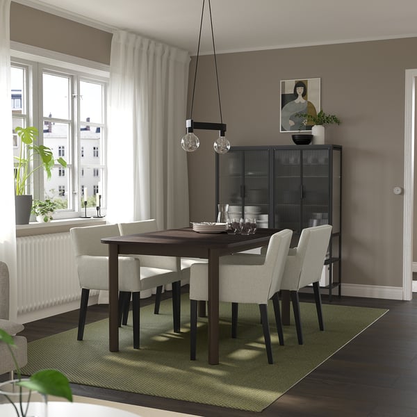 Modern dining room with STRANDTORP table, eight chairs, pendant lights, dark cabinet, large window, and green rug. Contemporary decor.