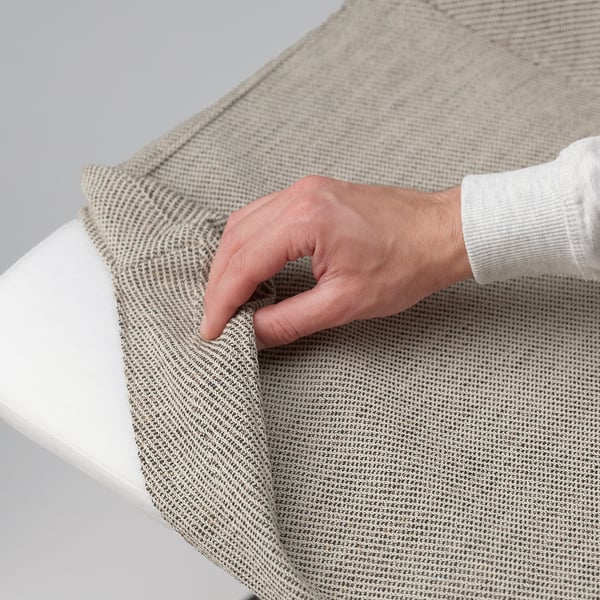 Hand folding tan textured fabric over edge of white table.