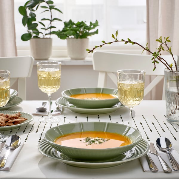 Table set with green STRIMMIG bowls, white wine glasses, silver cutlery, and plant centrepieces.