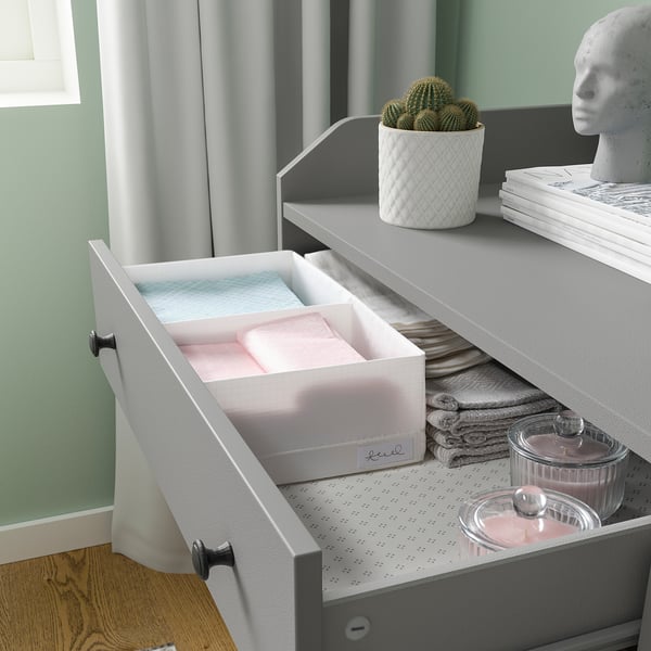 Open drawer with STUK boxes and tupperware, grey drawer, white curtains, cactus plant, elegant decor.