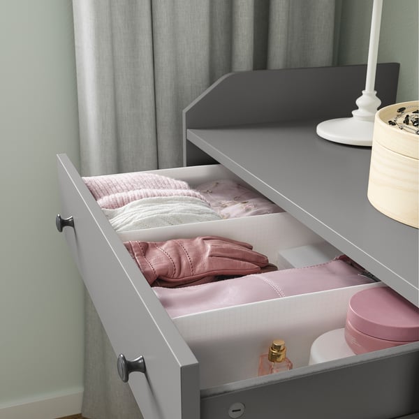Open gray drawer with white dividers, pink clothes, and accessories inside.