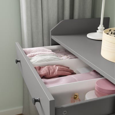 Open gray drawer with white dividers, pink clothes, and accessories inside.