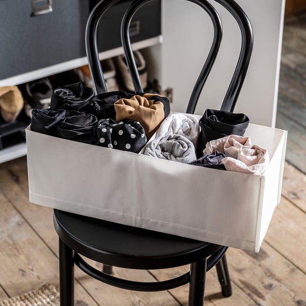 White organizer box on black chair, holding rolled socks in black, beige, white, and gray.