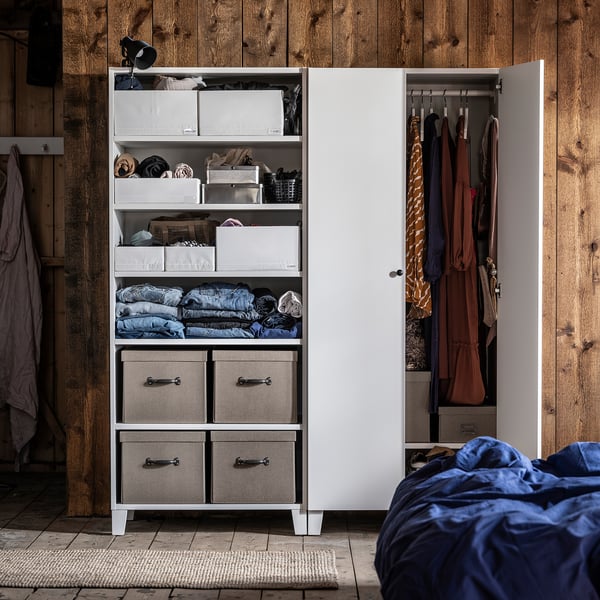 Modern white wardrobe with grey fabric storage boxes, neat clothes inside, set against wooden wall.
