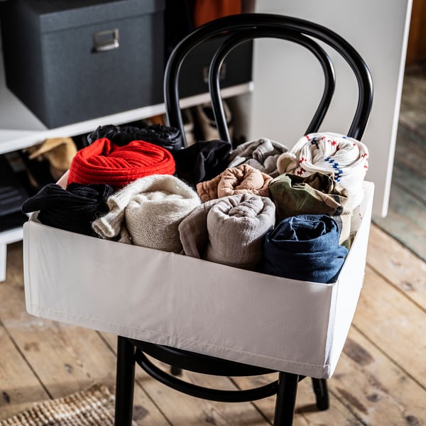 White storage basket with black handles, filled with colorful socks, on wooden floor.