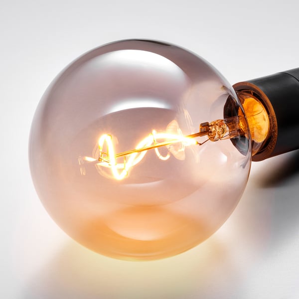 Close-up of a vintage-style bulb, glowing warmly in a smoked glass enclosure. Visible is the intricate spiral filament.