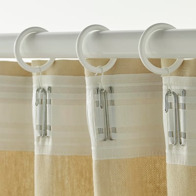 Three white curtain rings with hooks attached to a beige curtain.