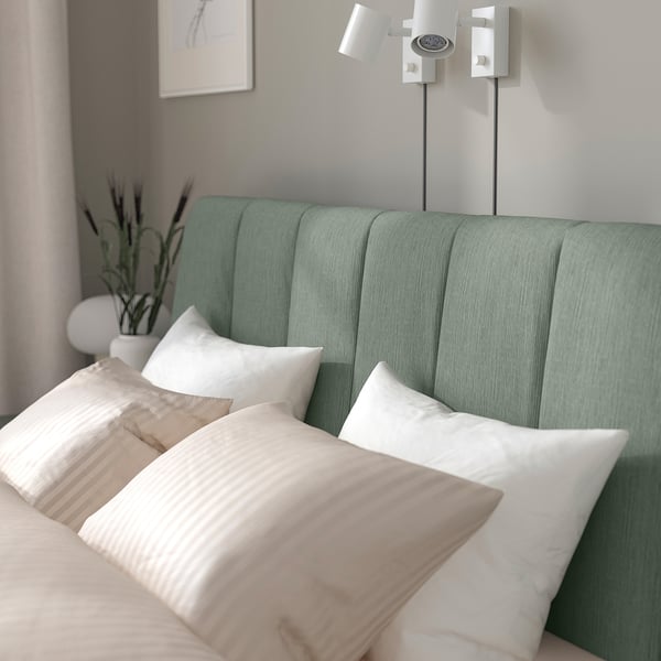 Modern bed with grey-green headboard, light beige bedding, and wall-mounted lights. Padded headboard leans against, soft and inviting.