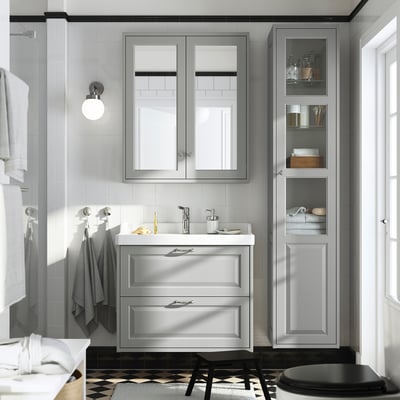 Modern grey bathroom with TÄNNFORSEN vanity, mirrored cabinet, hanging towels, and black stool. Vanity fits under tall cabinet, white countertop.
