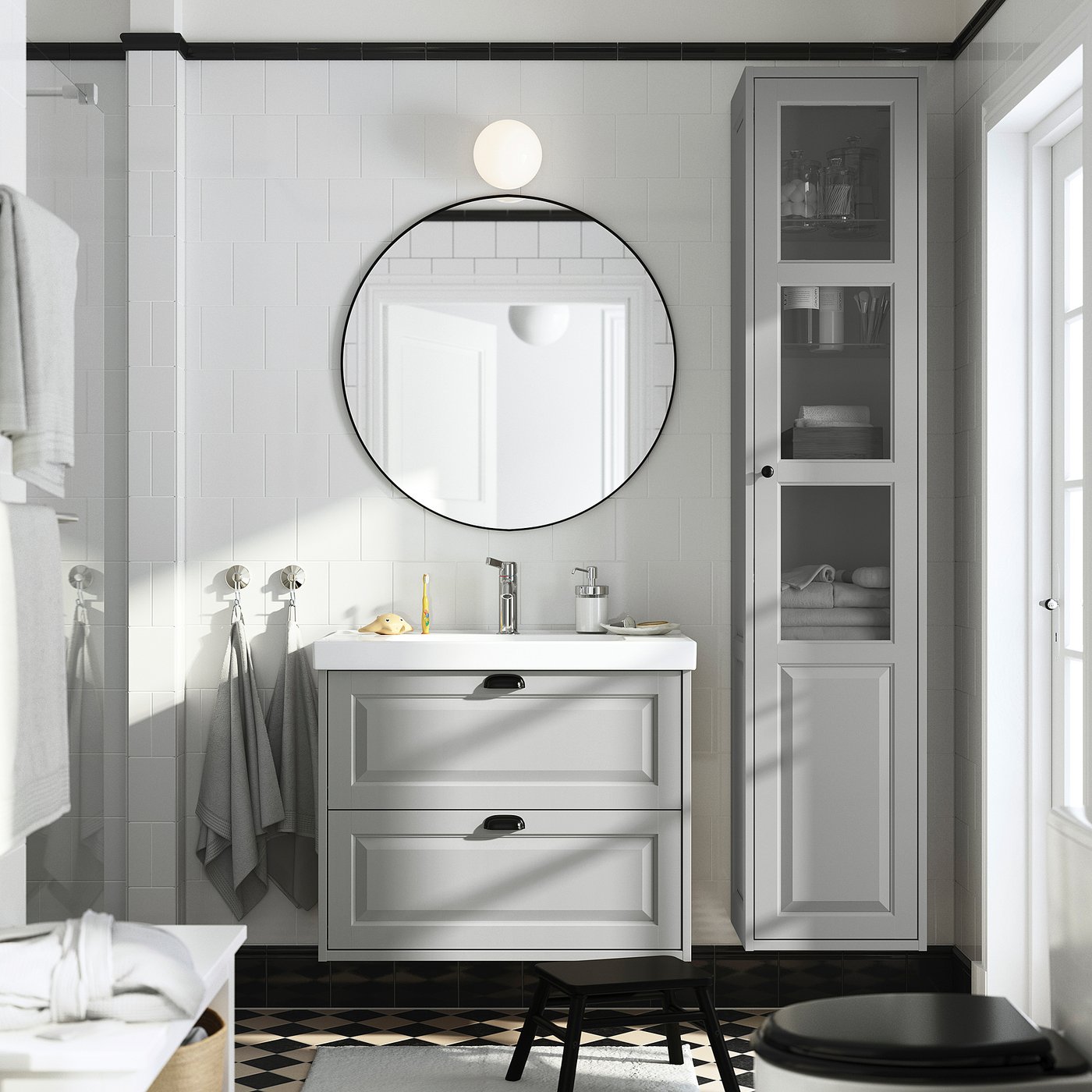 Grey bathroom, round mirror, TÄNNFORSEN vanity, white sink, grey towel, tall cabinet, black accents.