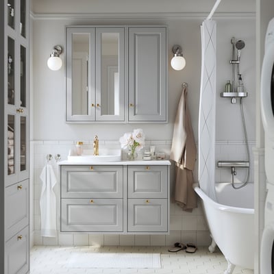 Modern grey vanity with drawers, marble counter, gold handles, & wall faucets. White tiles & tub. Spacious.