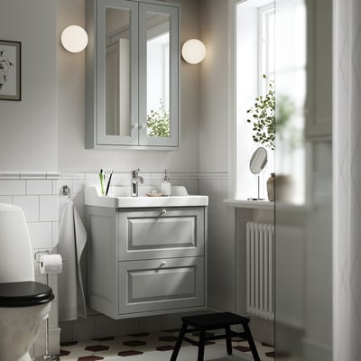 Modern grey bathroom with TÄNNFORSEN vanity, silver accents, sink, mirror, round lights, stool, plant, black/white floor.