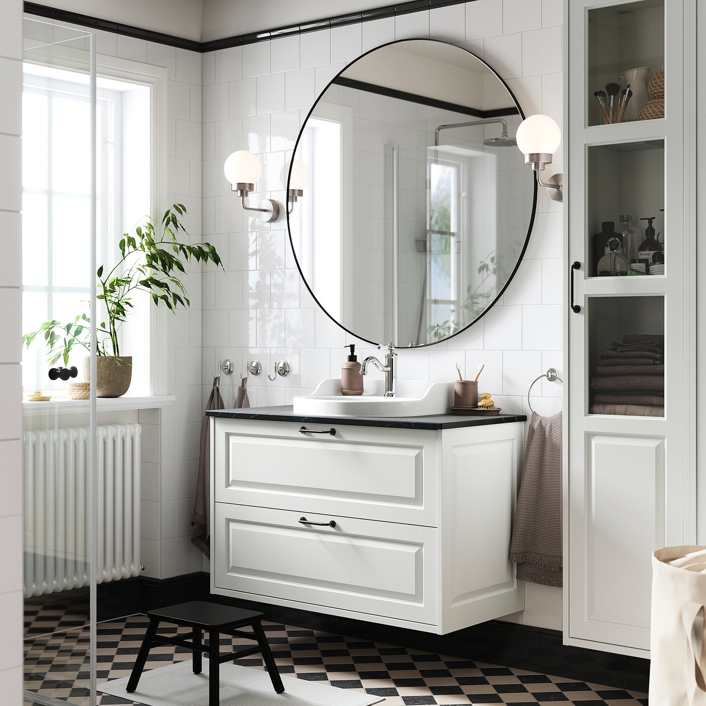 Modern bathroom with TÄNNFORSEN white vanity, round mirror, black chequered floor, and potted plant.