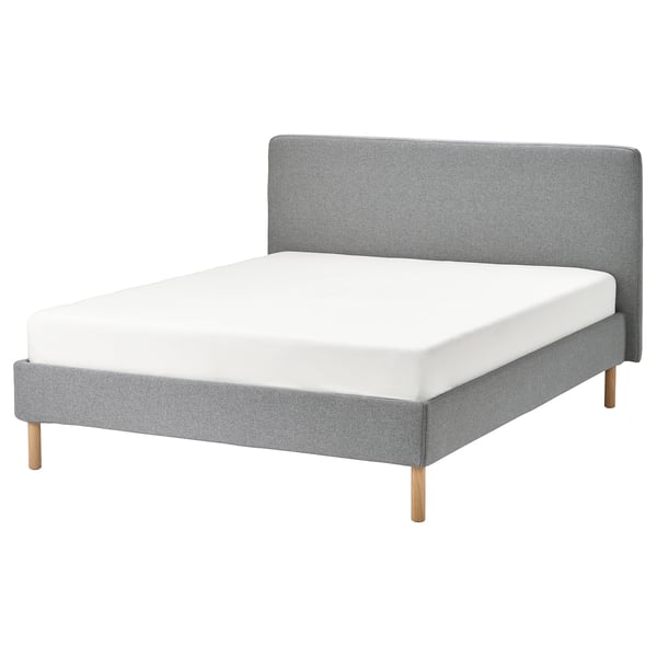 A TÄRNKULLEN bed frame in grey with a white mattress, featuring a soft padded headboard and wooden legs.