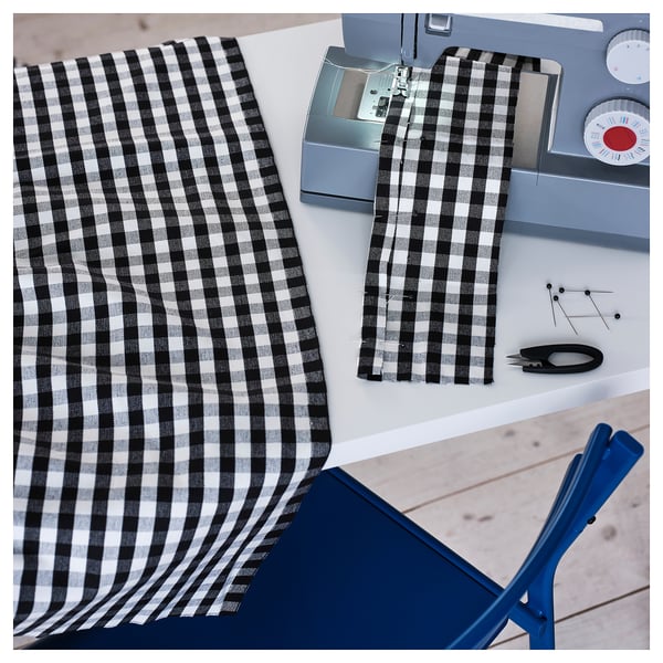 Black/white chequered fabric being sewn on a machine, with scissors and pins nearby.