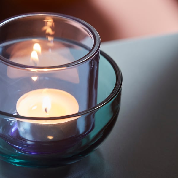 Lit tealight in elegant glass holder, casting warm glow, placed on smooth surface.