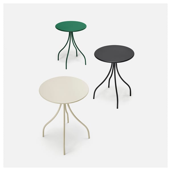 Three colourful round tables with thin, curved legs arranged in a triangular formation; green top, black top, beige bottom.