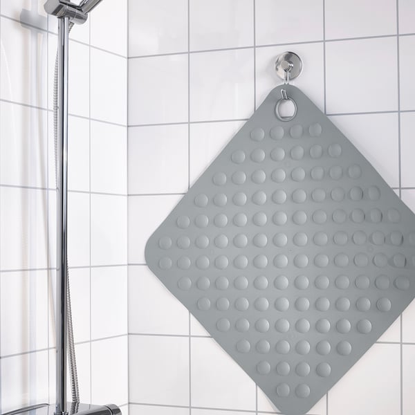 Grey square shower mat with suction cups hangs on wall hook for drying.