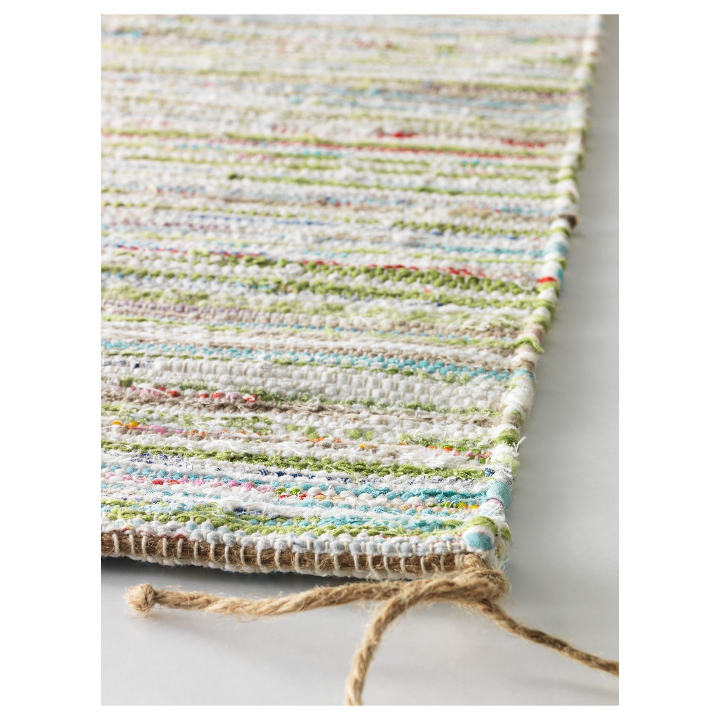 Handwoven rug with varied colours and textures; natural cotton fibres, braided edges, fringe ends.