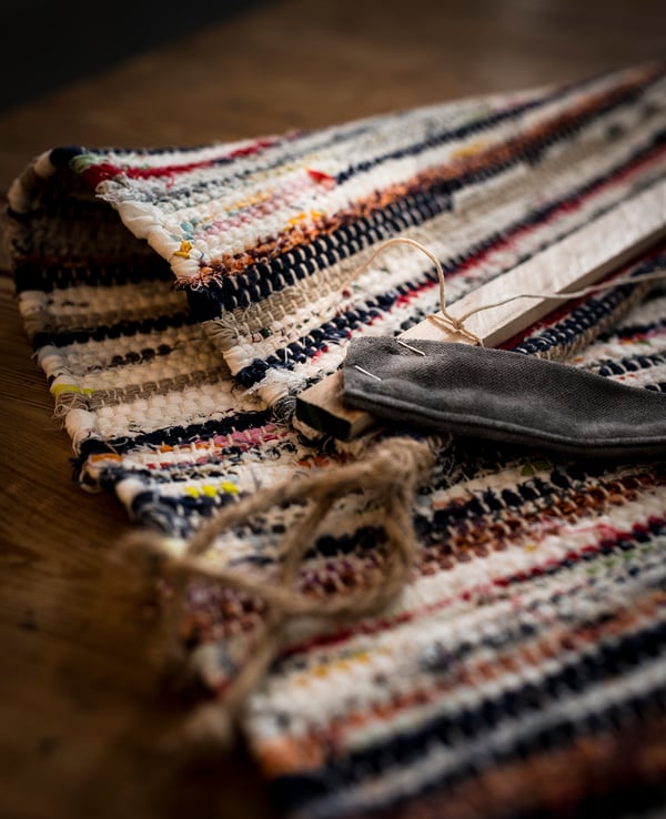 Handwoven multicoloured TÅNUM rug, featuring varied stripes of black, white, red, and yellow on a wooden floor.