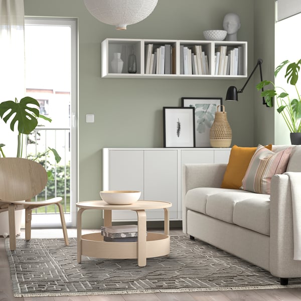 Modern living room with light green walls, white sofa, wooden coffee table, patterned rug, and bookshelf.