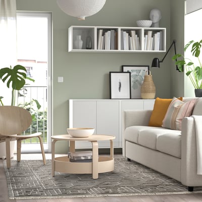 Modern living room with light green walls, white sofa, wooden coffee table, patterned rug, and bookshelf.