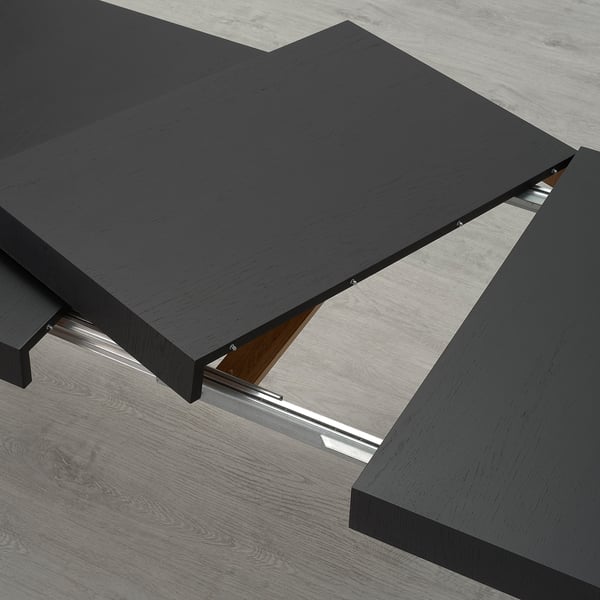 Black veneer extendable dining table with metal supports, shown with extra leaf stored underneath, seats 6-8.