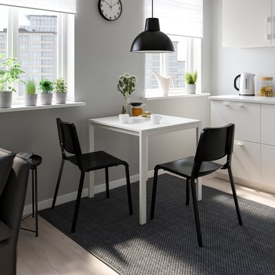 Minimalist kitchen with white table, black TEODORES chairs, hanging light, plants, and white cabinets. Chairs are lightweight and stackable.