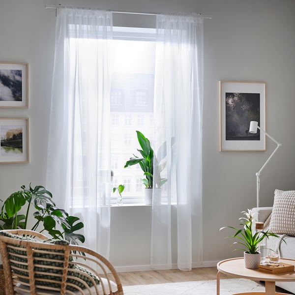 Bright living room with large TERESIA sheer white curtains covering a big window, flanked by plants and framed art, creating a spacious and airy feel.