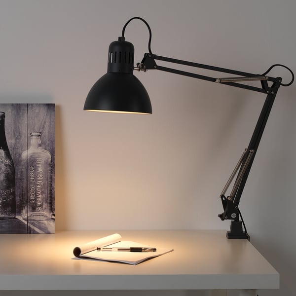 Black adjustable desk lamp TERTIAL illuminates a work space with paper and pen.