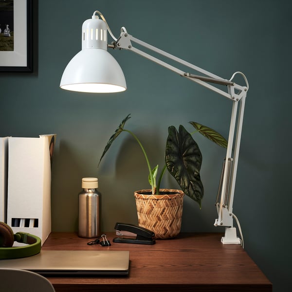 White TERTIAL lamp on wooden desk, illuminating plant and office supplies.
