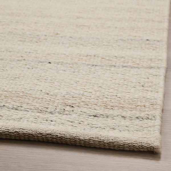Close-up of cream-colored, handcrafted wool rug. Textured, high-quality fibres visible.