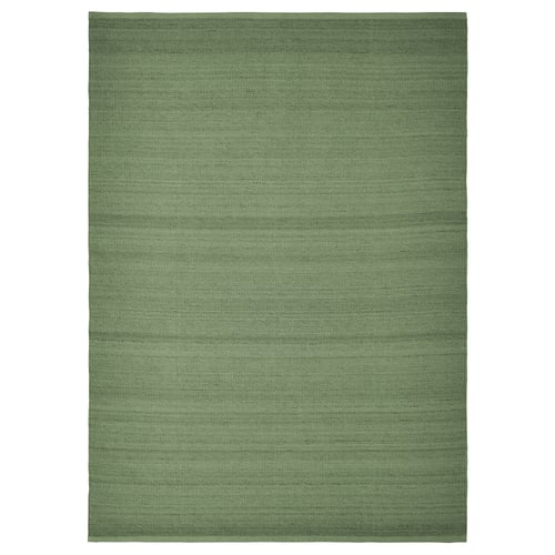 This image shows the TIDTABELL, a green rectangular rug with a wool surface and cotton backing. Its flatwoven and a subtle melange pattern.