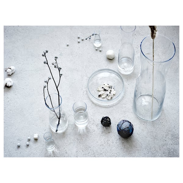 Glass vases of various shapes and sizes on a concrete surface, some containing dried branches and decorative items.