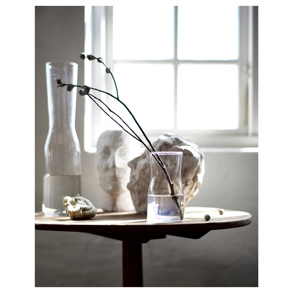 Clear glass vase with long-stemmed flowers and textured white vases on a table by a window.
