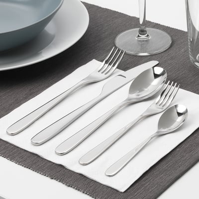 Silver cutlery set on napkin: fork, knife, spoon, teaspoon, arranged neatly.