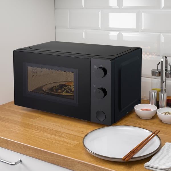Black TILLREDA microwave on wooden counter with plate & chopsticks.