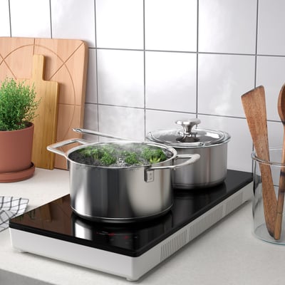 Modern induction hob with two pots cooking vegetables, set on a sleek kitchen counter. It touch controls and uses magnetic cookware.