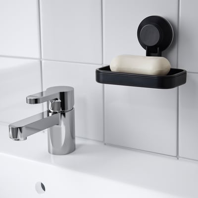 Small black TISKEN soap dish suctioned to tiled wall beside shiny chrome faucet, holding white soap.
