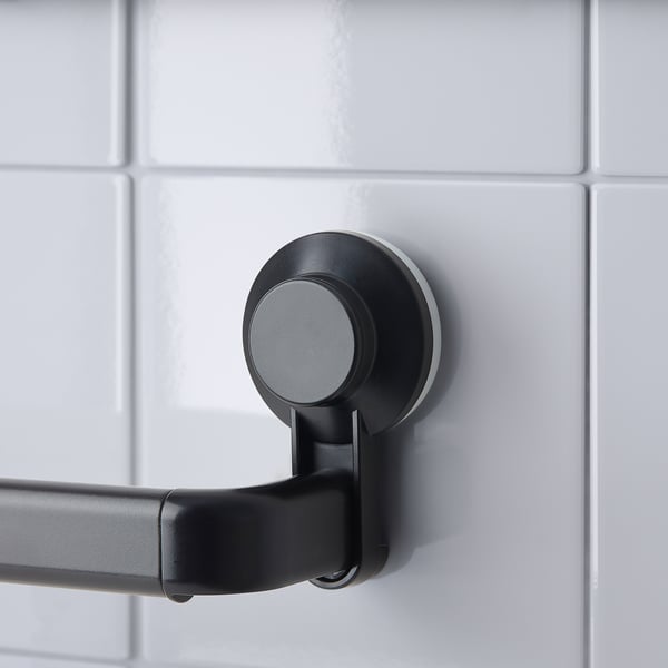 Black extendable towel rack with suction cup mounted on tiled wall.