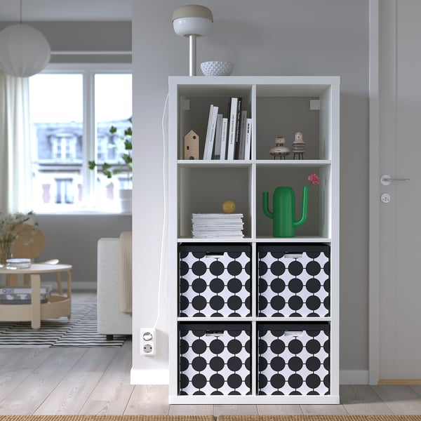 White TJENA box with black dots on shelf among books and decor.