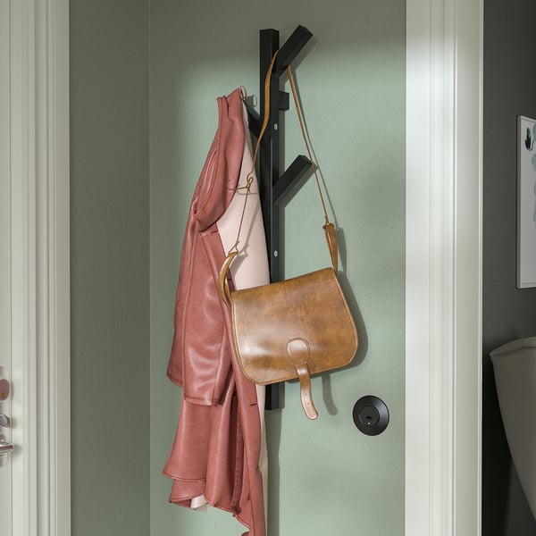 Wooden coat rack holds pink jacket & brown bag by white door.