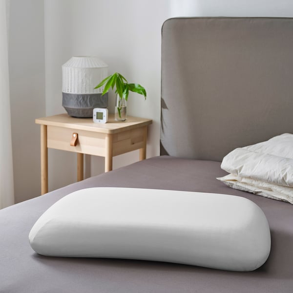 Modern bedroom with ergonomic pillow, bedside table with lamp and plant.