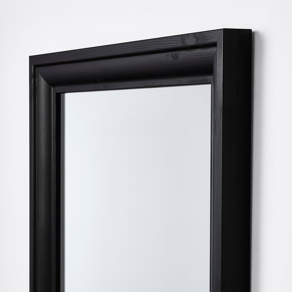 Black-framed mirror with moulded edges, hanging vertically on a wall, reflecting light.
