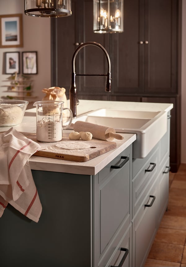 Modern kitchen with dark cabinets, light countertop, white sink, black tap, rolling pin, and measuring cup with flour.